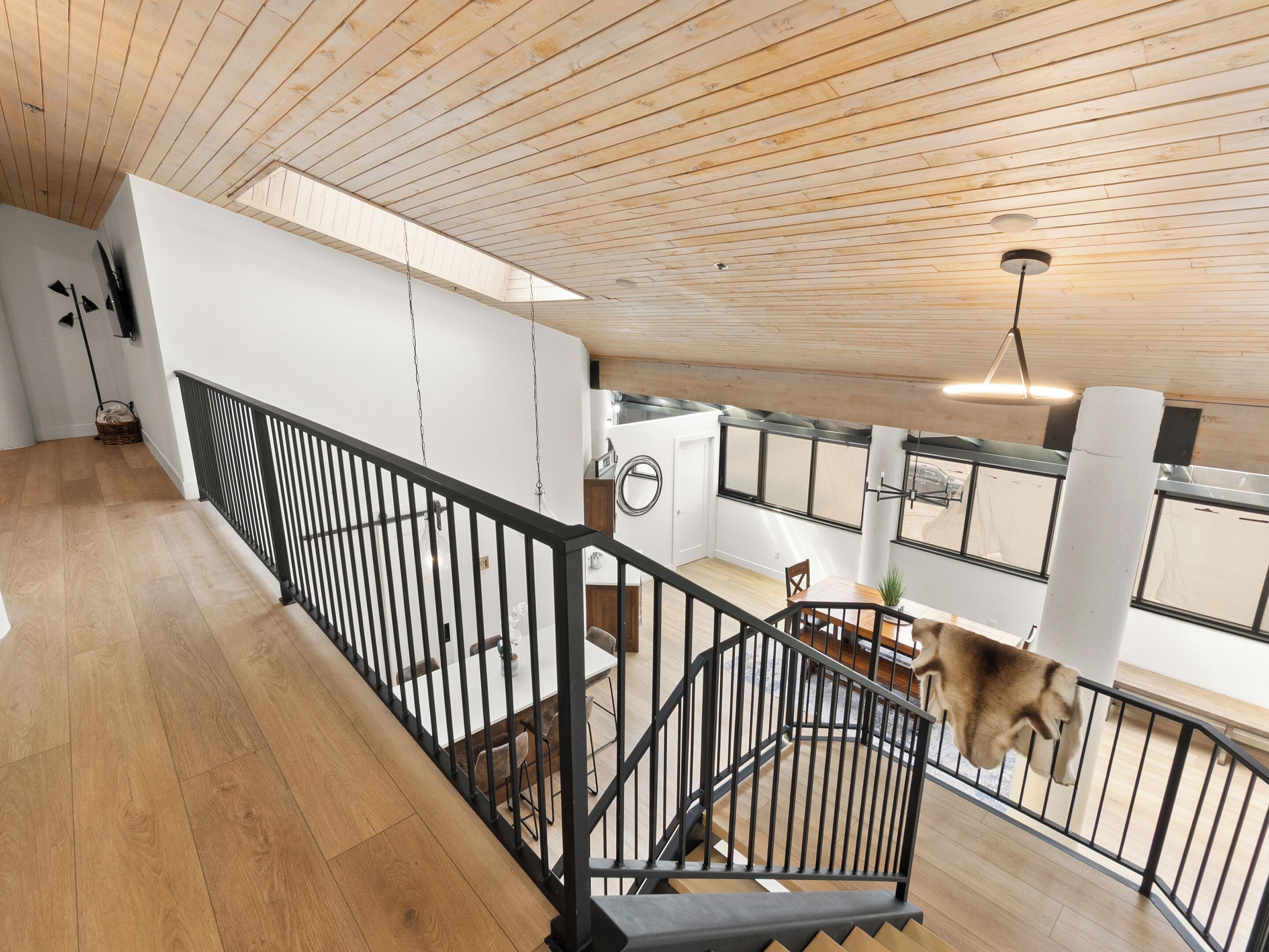 Ein geräumiger Innenraum mit Holzbalkendecke, einer Treppe mit schwarzen Geländern und einem Essbereich mit Tisch und Stühlen.