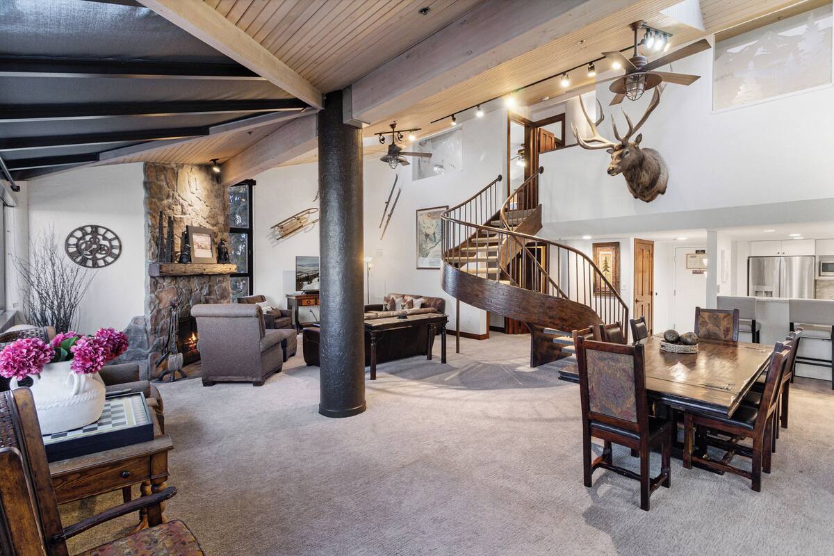 Un espacio habitable amplio con una escalera de madera, una mesa de comedor y una chimenea.