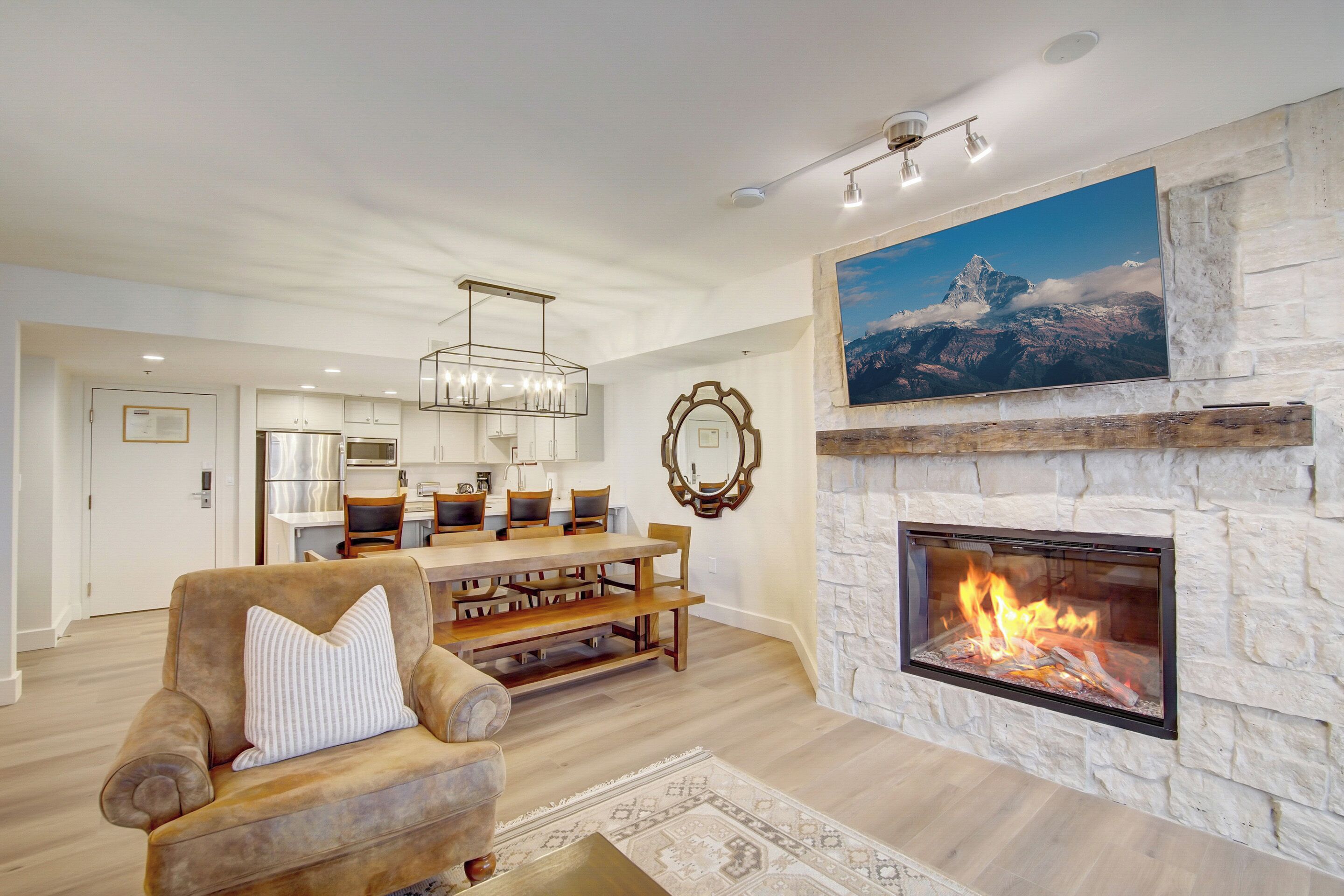 A modern living room with a stone fireplace, a dining area, and a kitchen in the background.