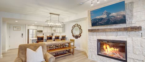 A modern living room with a stone fireplace, a dining area, and a kitchen in the background.