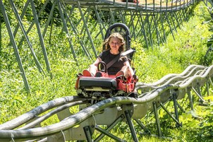 Eine Person auf einer Achterbahn, gesichert mit einem Sicherheitsgurt, umgeben von viel Grün.