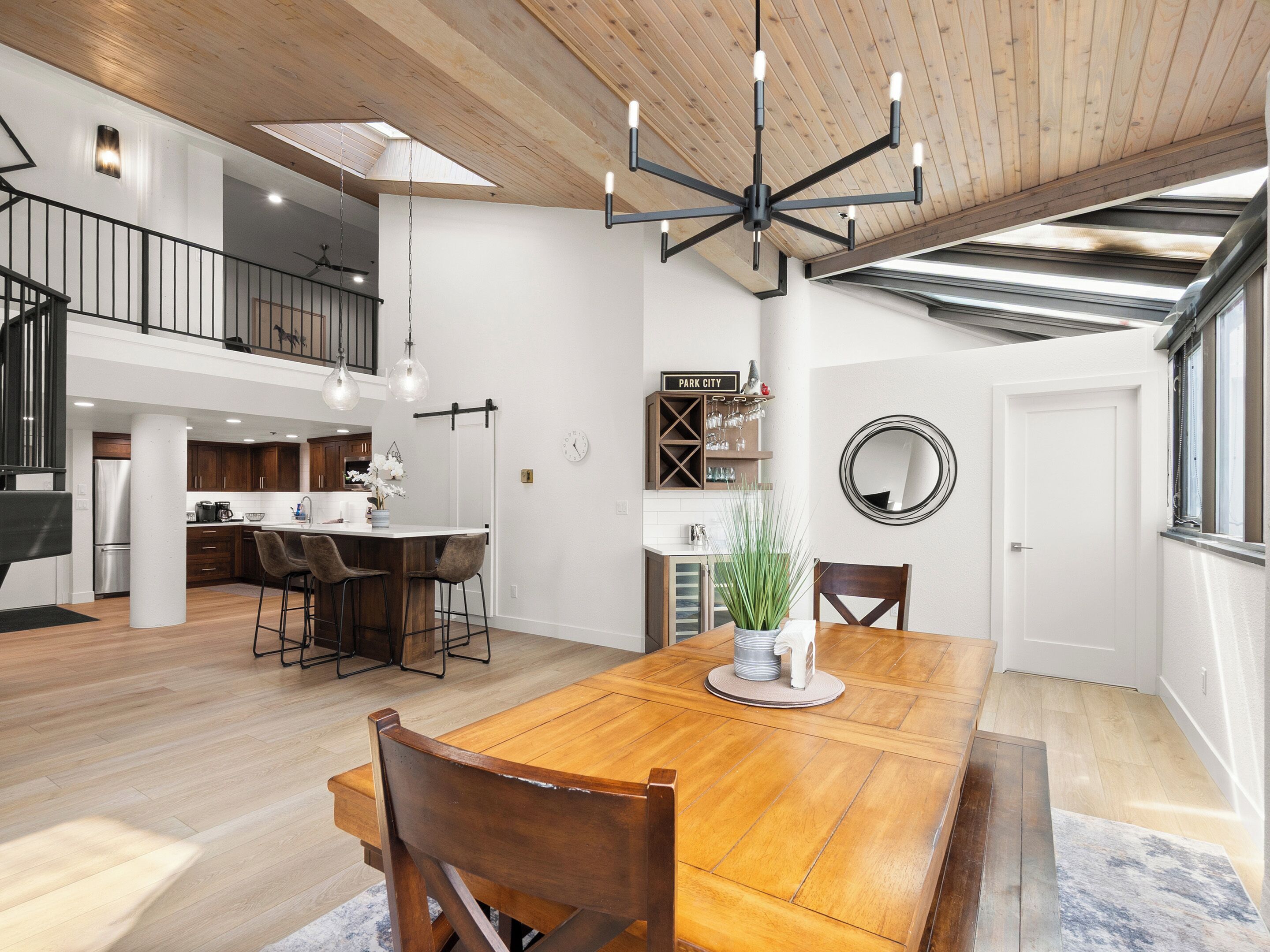 Una cocina amplia con una isla central, un comedor con mesa de madera y un dormitorio en lo alto con balcón.