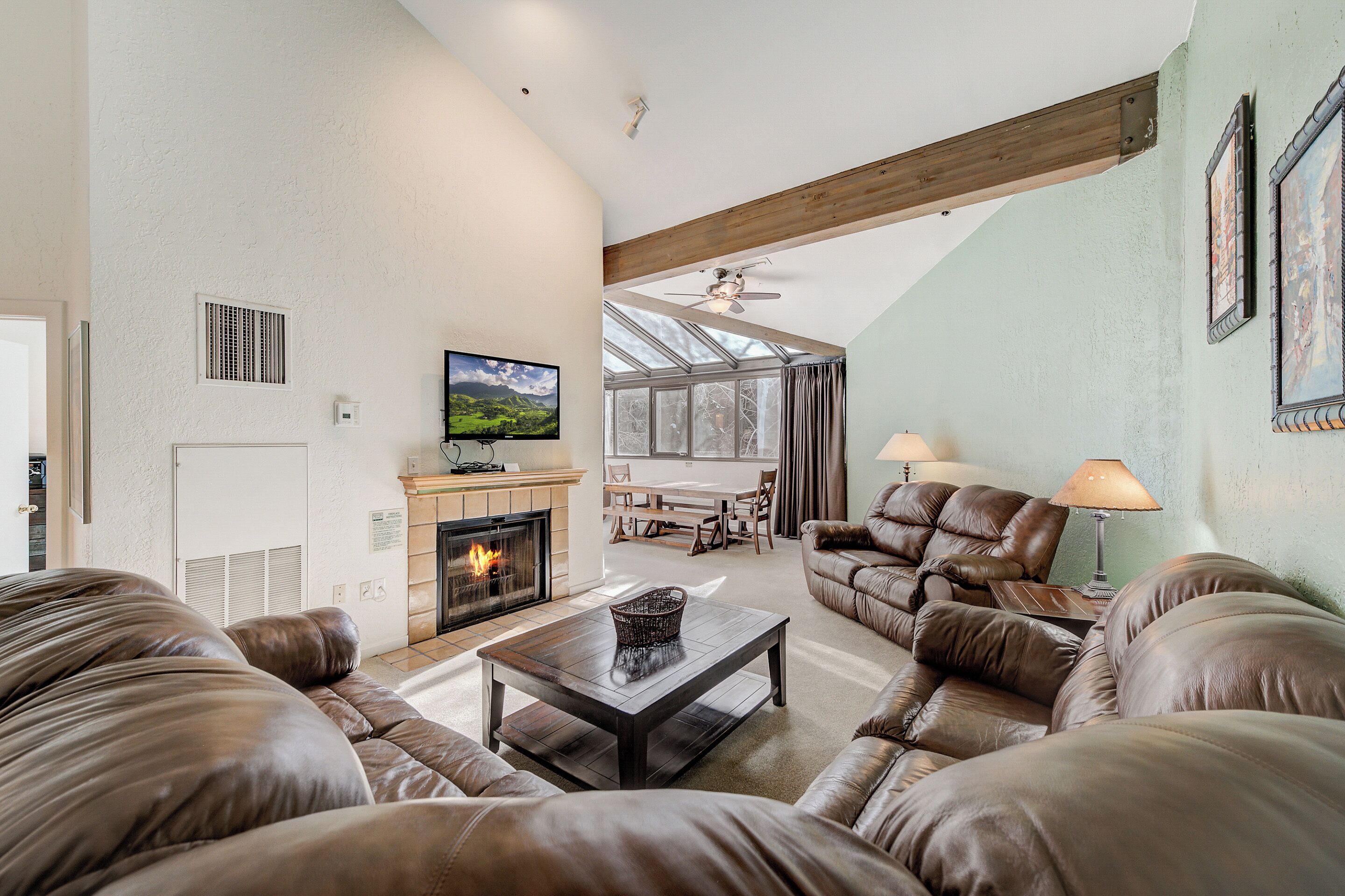 Ein geräumiges Wohnzimmer mit Ledersofas, einem Kamin, einem Fernseher und einem großen Fenster mit Vorhängen.