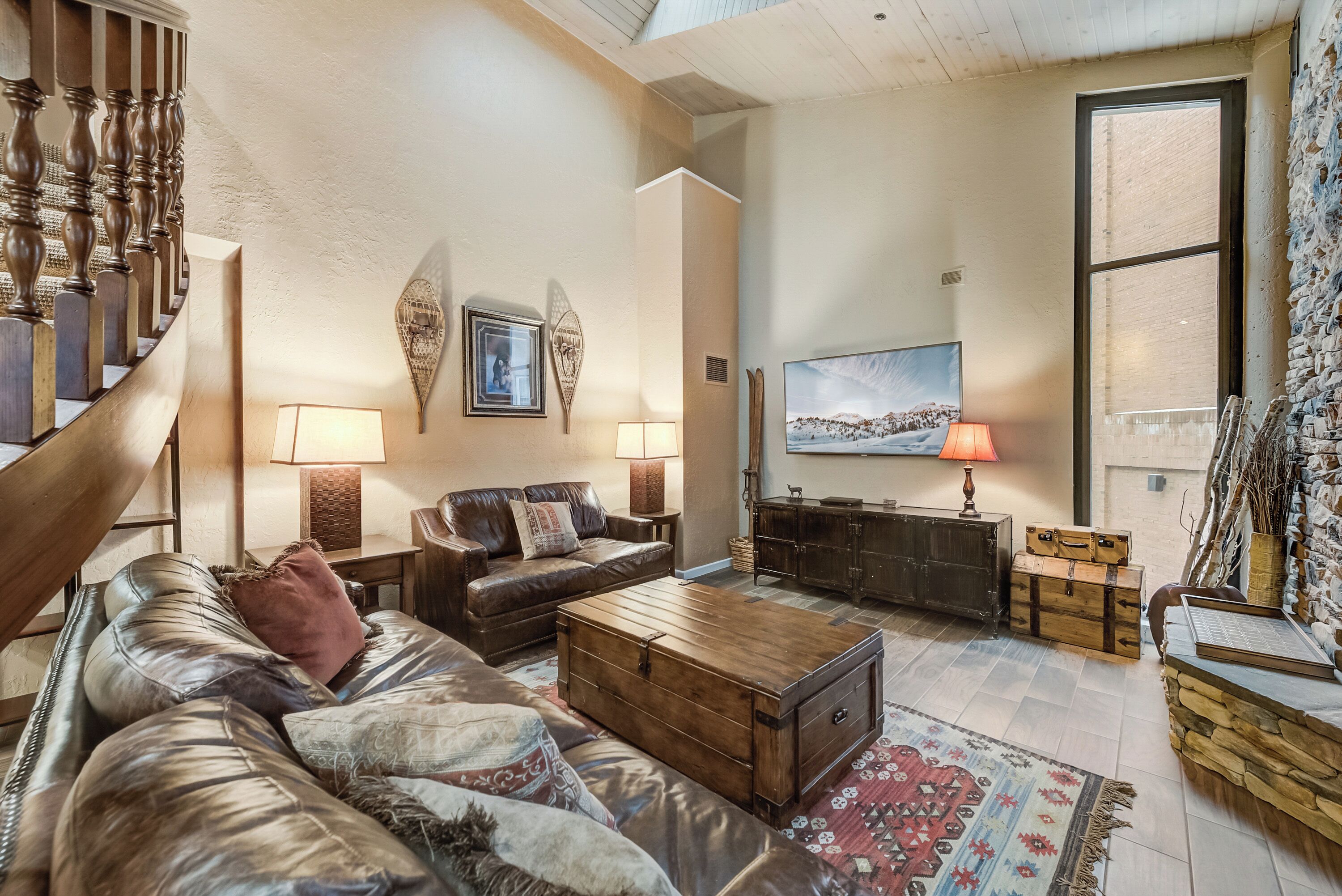 A spacious living room with a leather sofa, a wooden coffee table, and a large window with a scenic view.