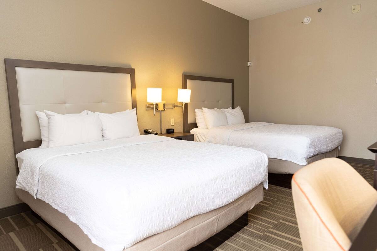 A hotel room with two beds, each with a headboard, bedside tables, and lamps.