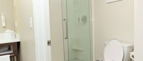 Ein Badezimmer mit einer Duschkabine aus Glas, einer weißen Toilette und einem Waschbecken mit Toilettenartikeln.