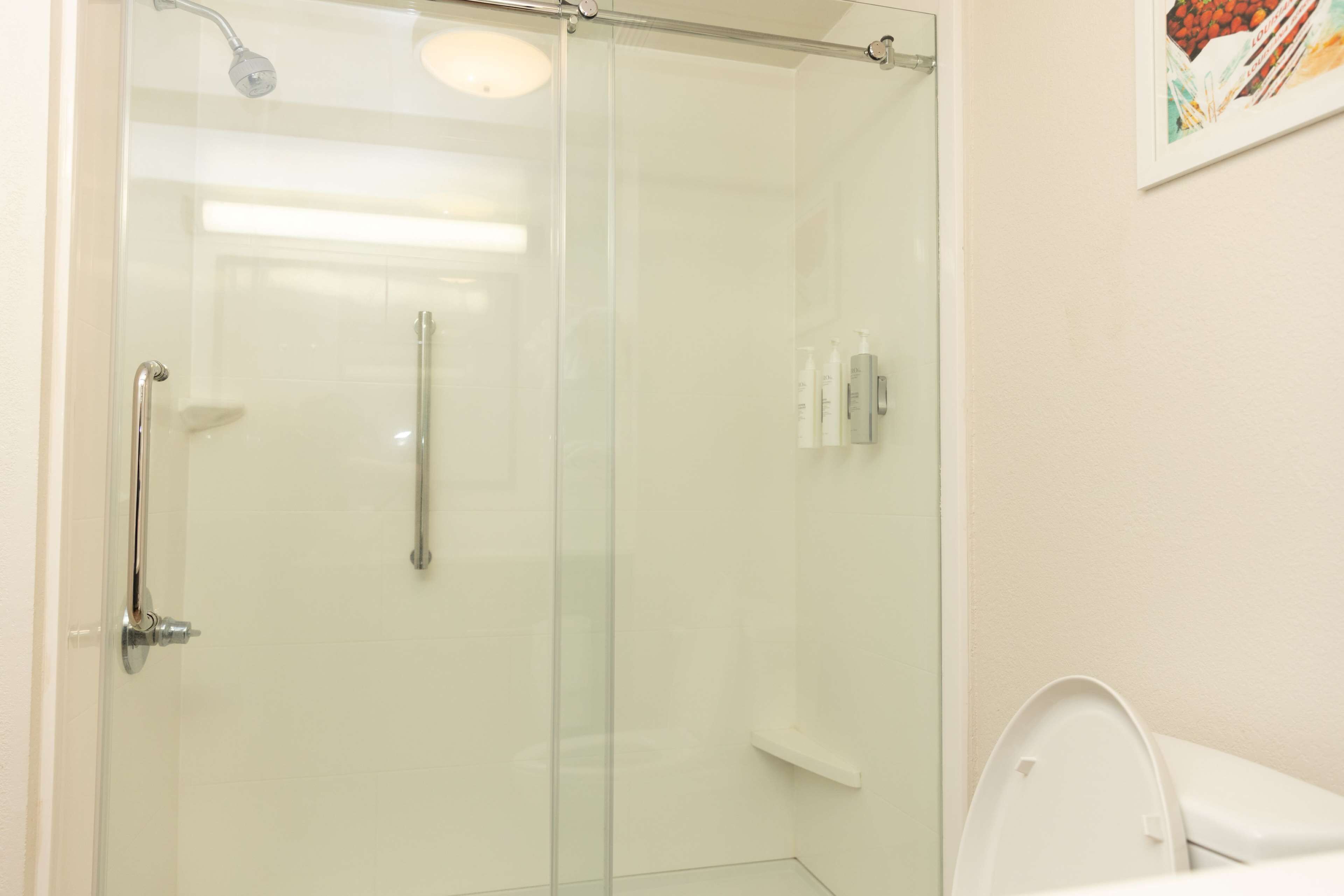 A modern bathroom with a glass shower enclosure, a white toilet, and a small shelf with toiletries.