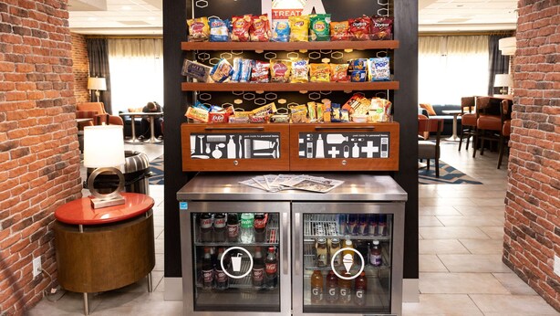 A snack display with various chips and a beverage cooler in a hotel lobby. - Hampton Inn Hammond (Hammond)