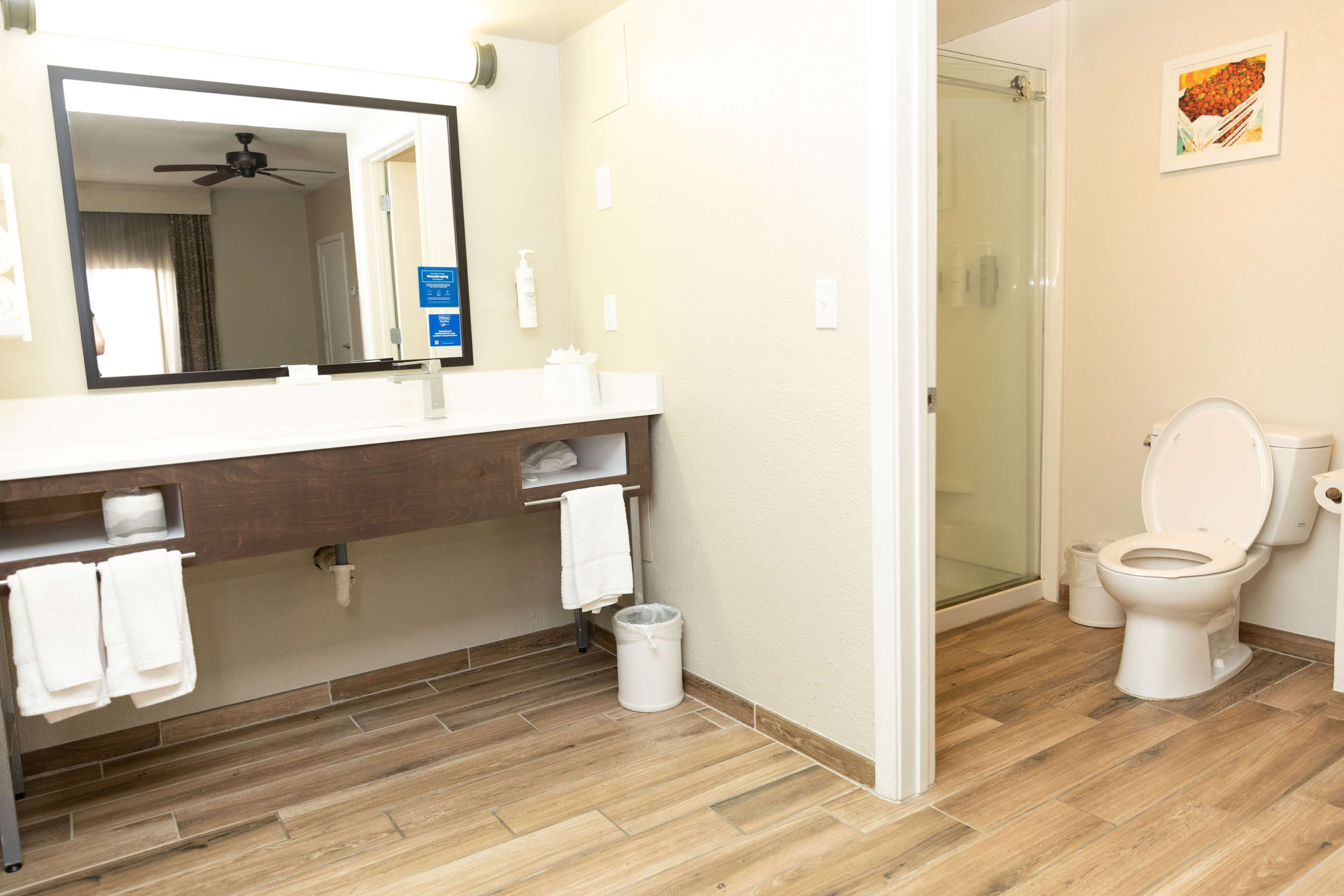 Une salle de bain moderne avec un plancher en bois, un lavabo blanc, un miroir, des toilettes et un espace douche.