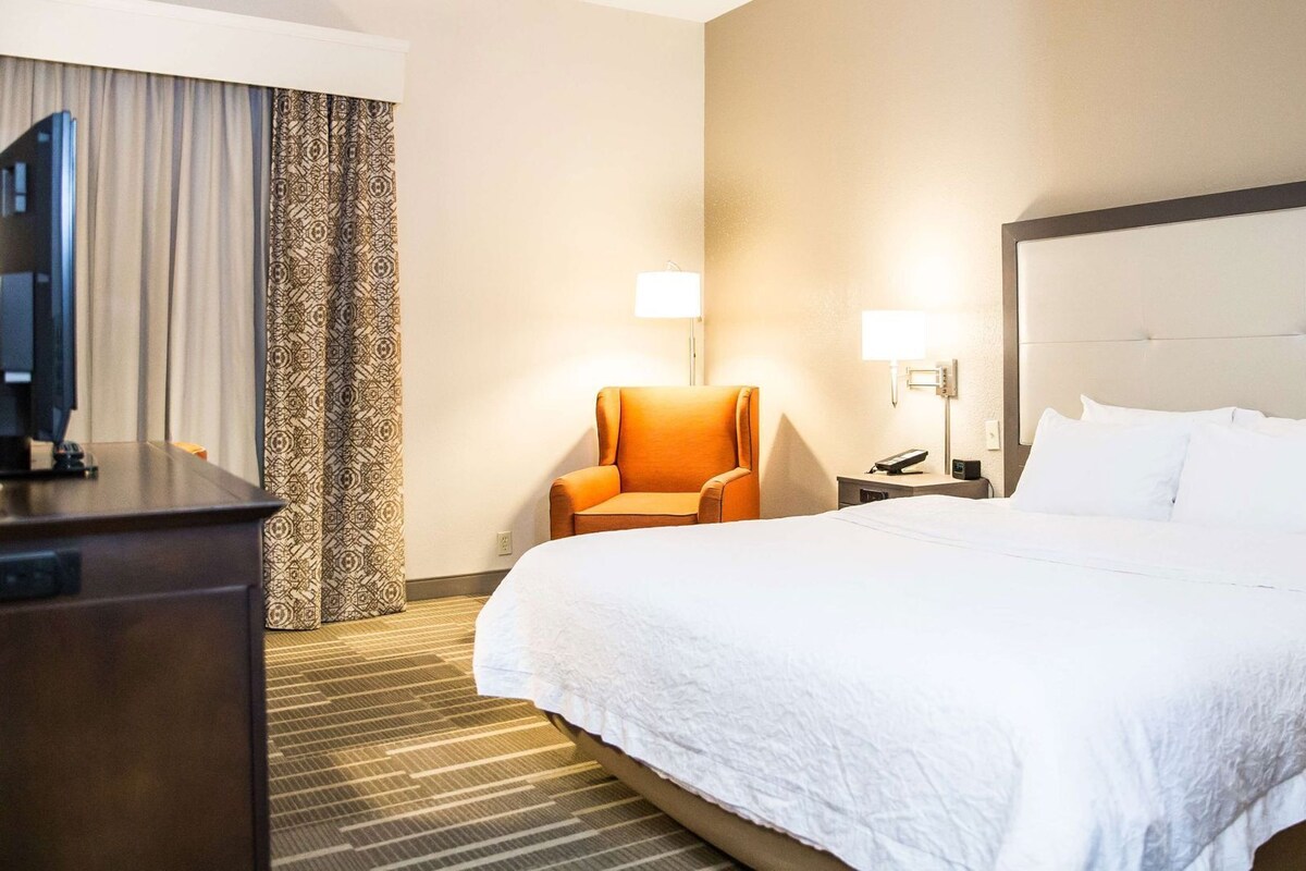 Una habitación de hotel con cama, escritorio, silla, televisor y lámpara.