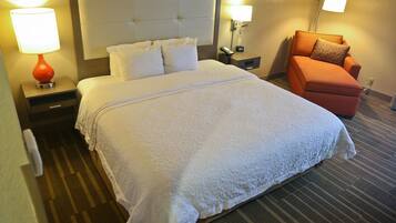 A hotel room with a large bed, two bedside tables, a nightstand, an orange armchair, and two wall-mounted lamps.