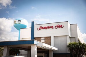 A Hampton Inn hotel with a prominent sign and a water tower with a logo.