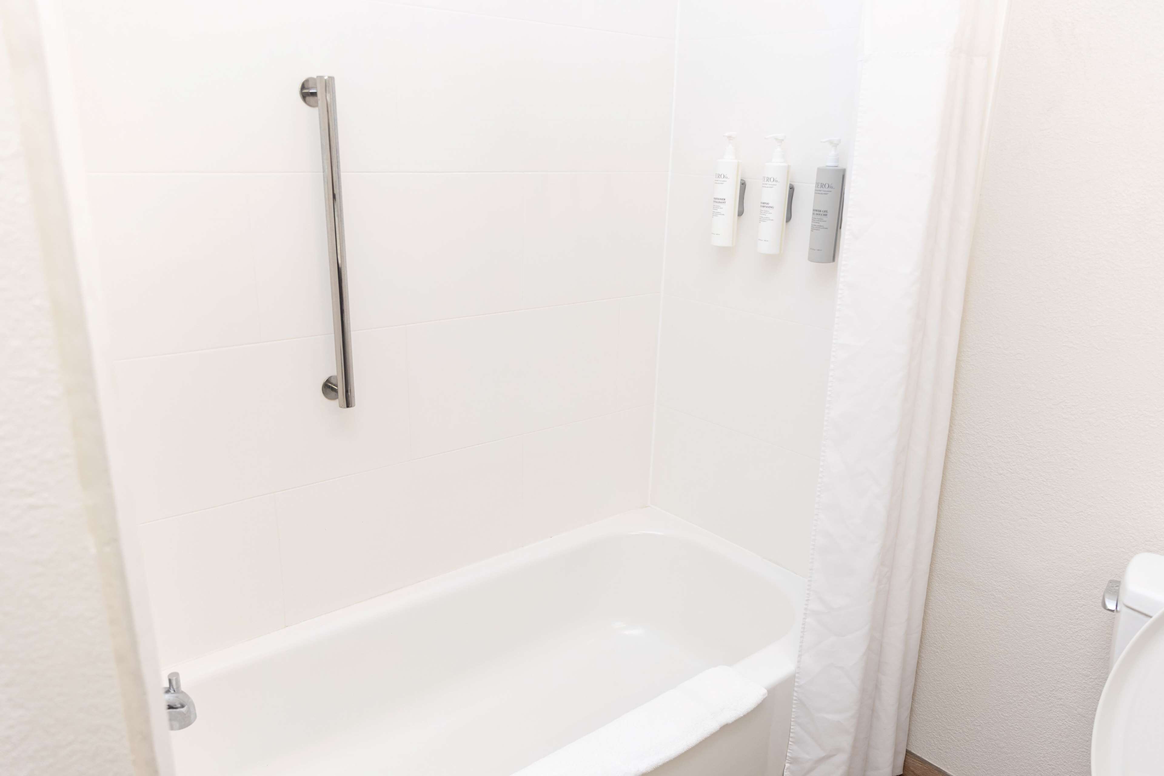 A bathroom with a white bathtub, a shower curtain, and toiletries on the wall.