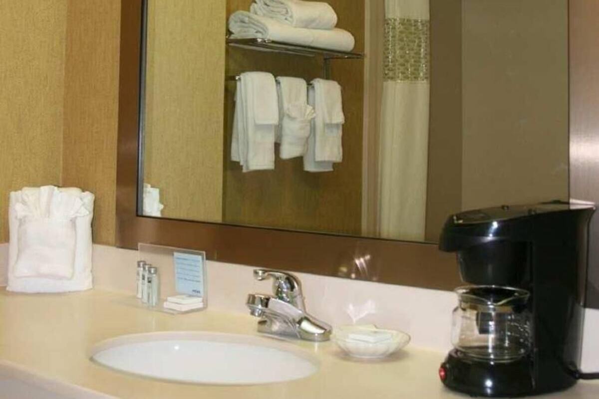 A hotel bathroom with a sink, mirror, towel rack, and a coffee maker.