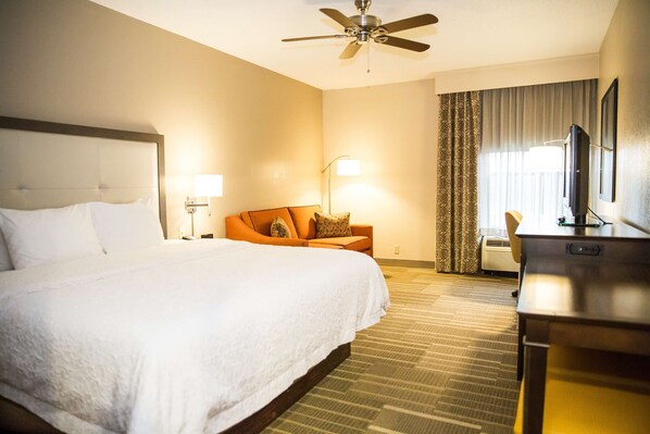 A hotel room with a large bed, a desk, a chair, a television, a ceiling fan, and a window with curtains. - Hampton Inn Hammond (Hammond)