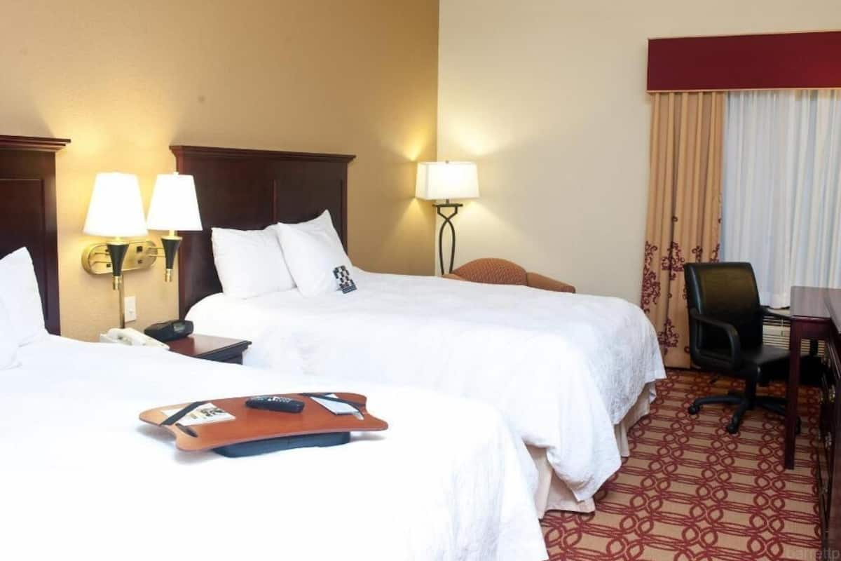 A hotel room with two beds, a desk, a chair, and lamps.