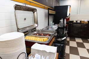 A buffet setup with various food items, including eggs and sausages, and a stack of white plates.