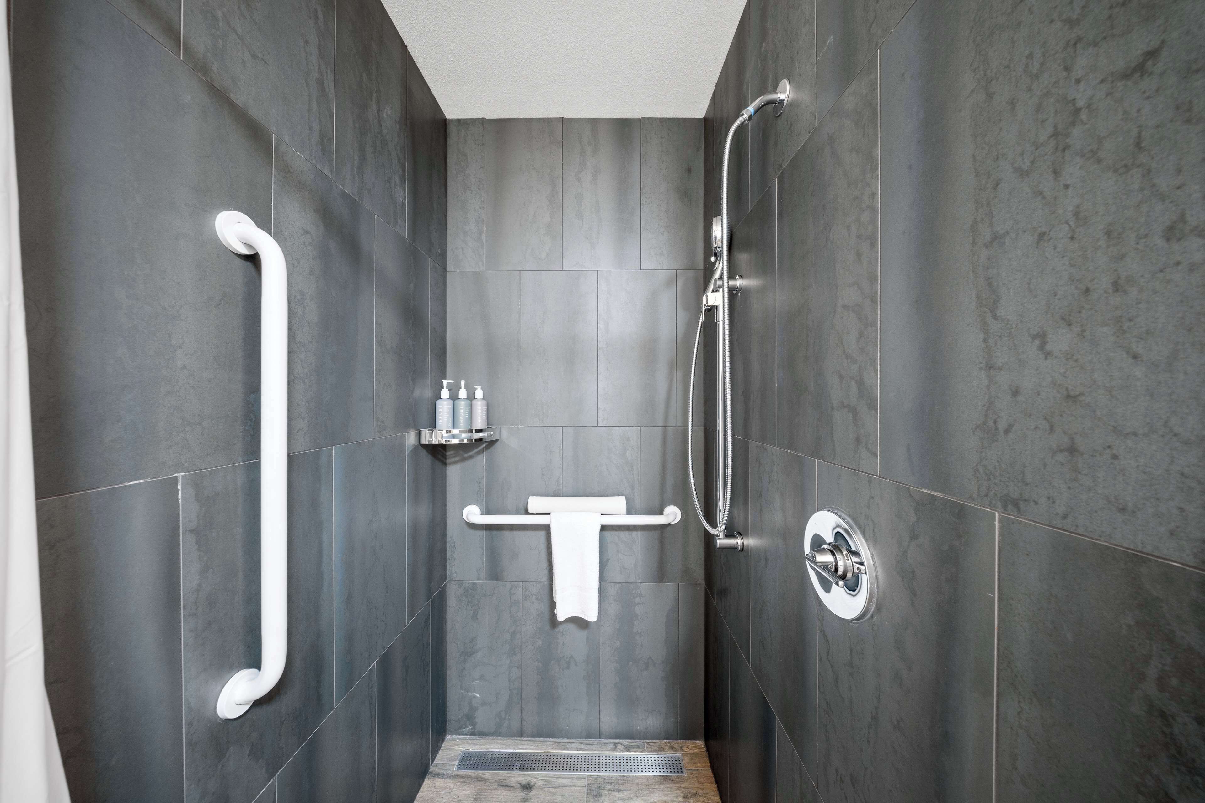 Un espace douche moderne équipé d’une barre d’appui, d’un porte-serviettes et d’un pommeau de douche.