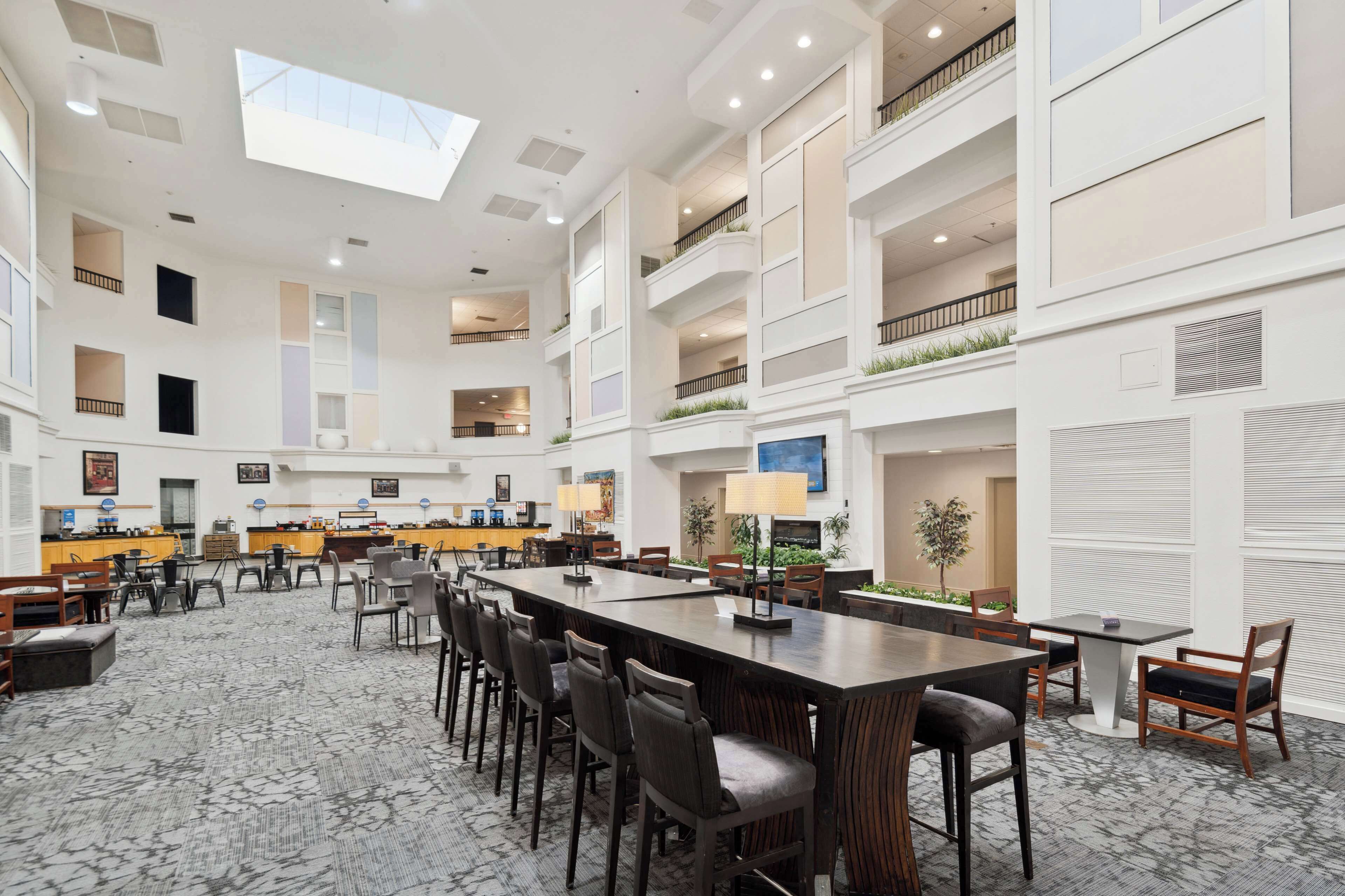 Un hall de hotel espacioso con techo alto, varias zonas de estar y una larga mesa central.