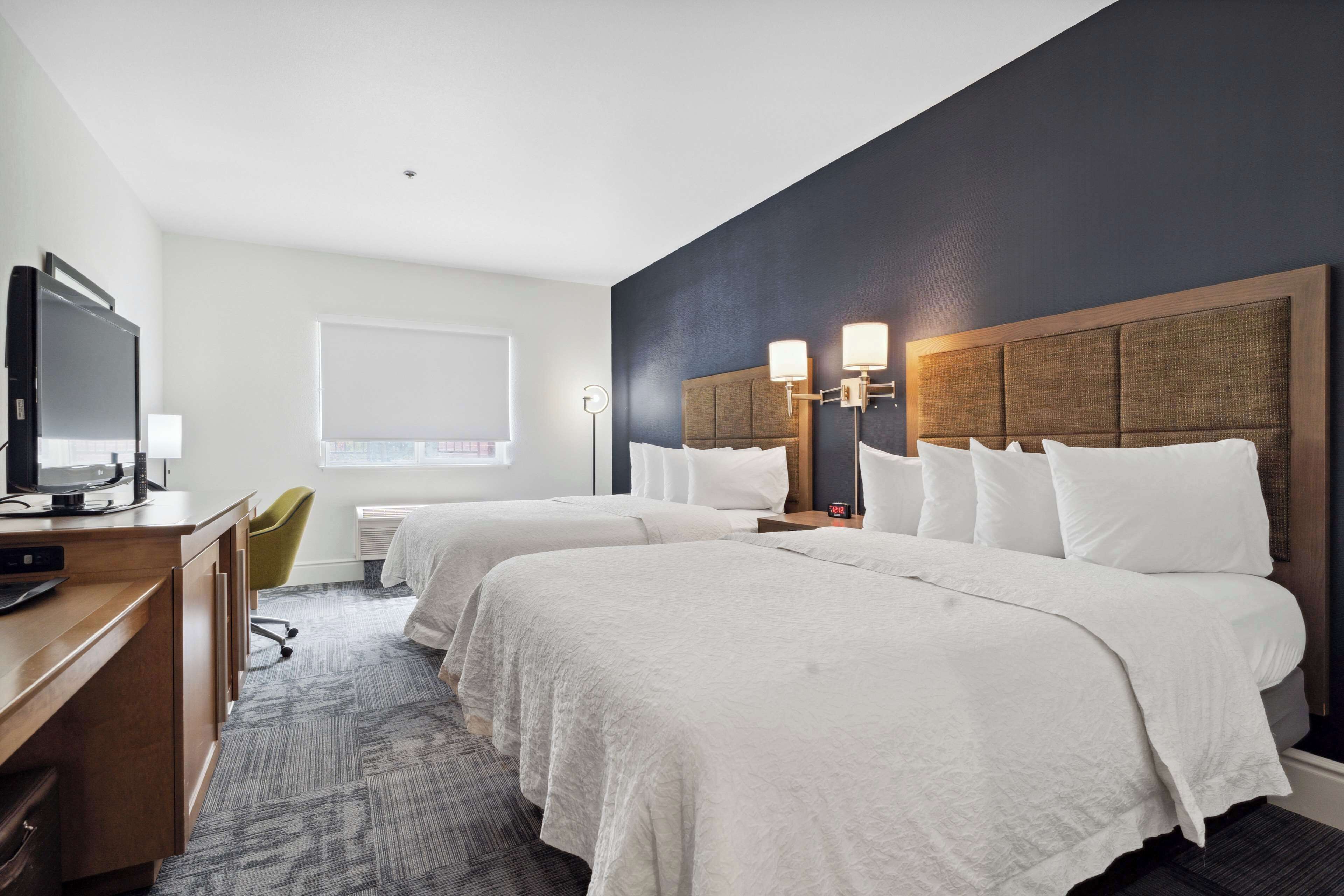 A hotel room with two beds, a desk with a computer, a chair, and a TV.