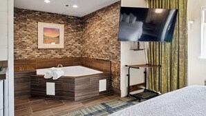 A modern bathroom with a stone wall, a large bathtub, a flat-screen TV, and a shower area. - Sonesta Essential Vacaville - Napa Valley (Vacaville)