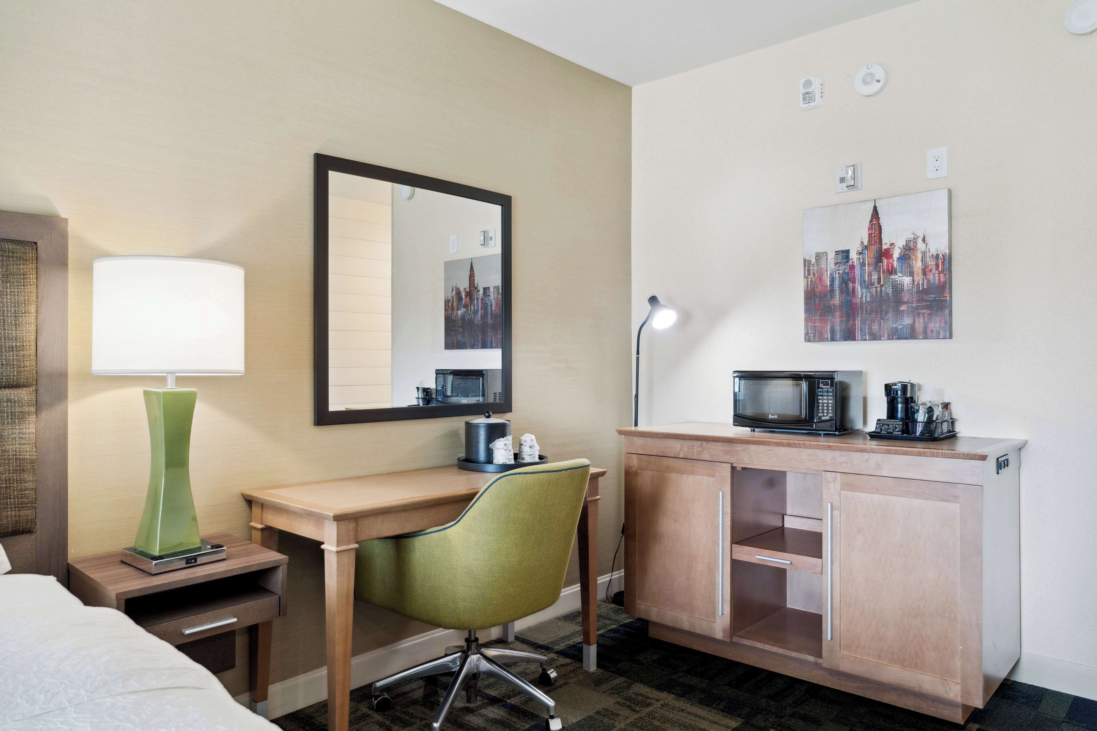 Habitación de hotel con cama, escritorio con silla, lámpara, microondas, cafetera y armario.