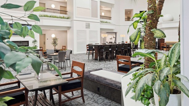 A spacious indoor atrium with multiple dining areas, high ceilings, and indoor plants. - Sonesta Essential Vacaville - Napa Valley (Vacaville)