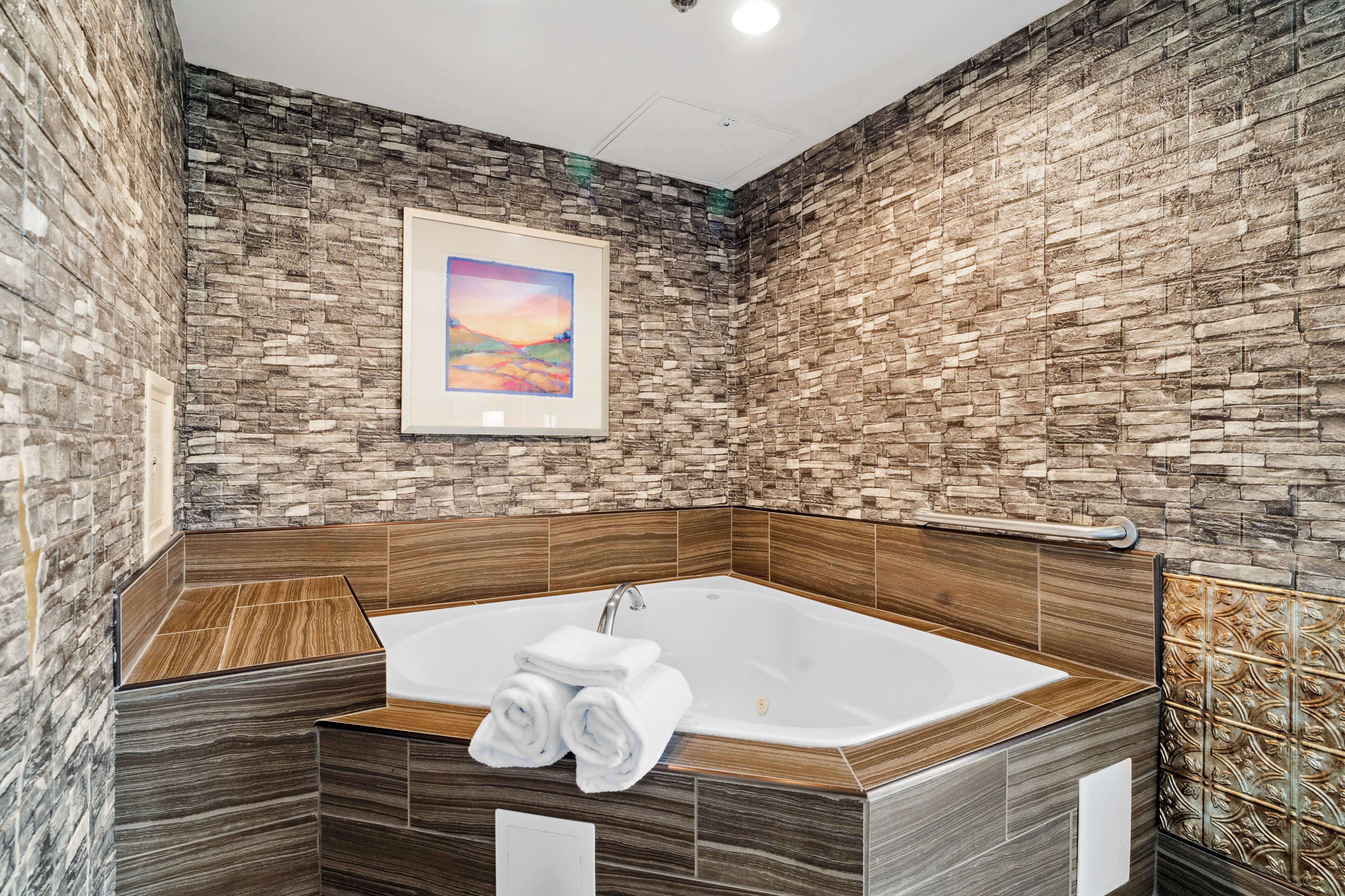 Un baño moderno con pared de piedra, un cuadro enmarcado y una bañera grande con toallas.