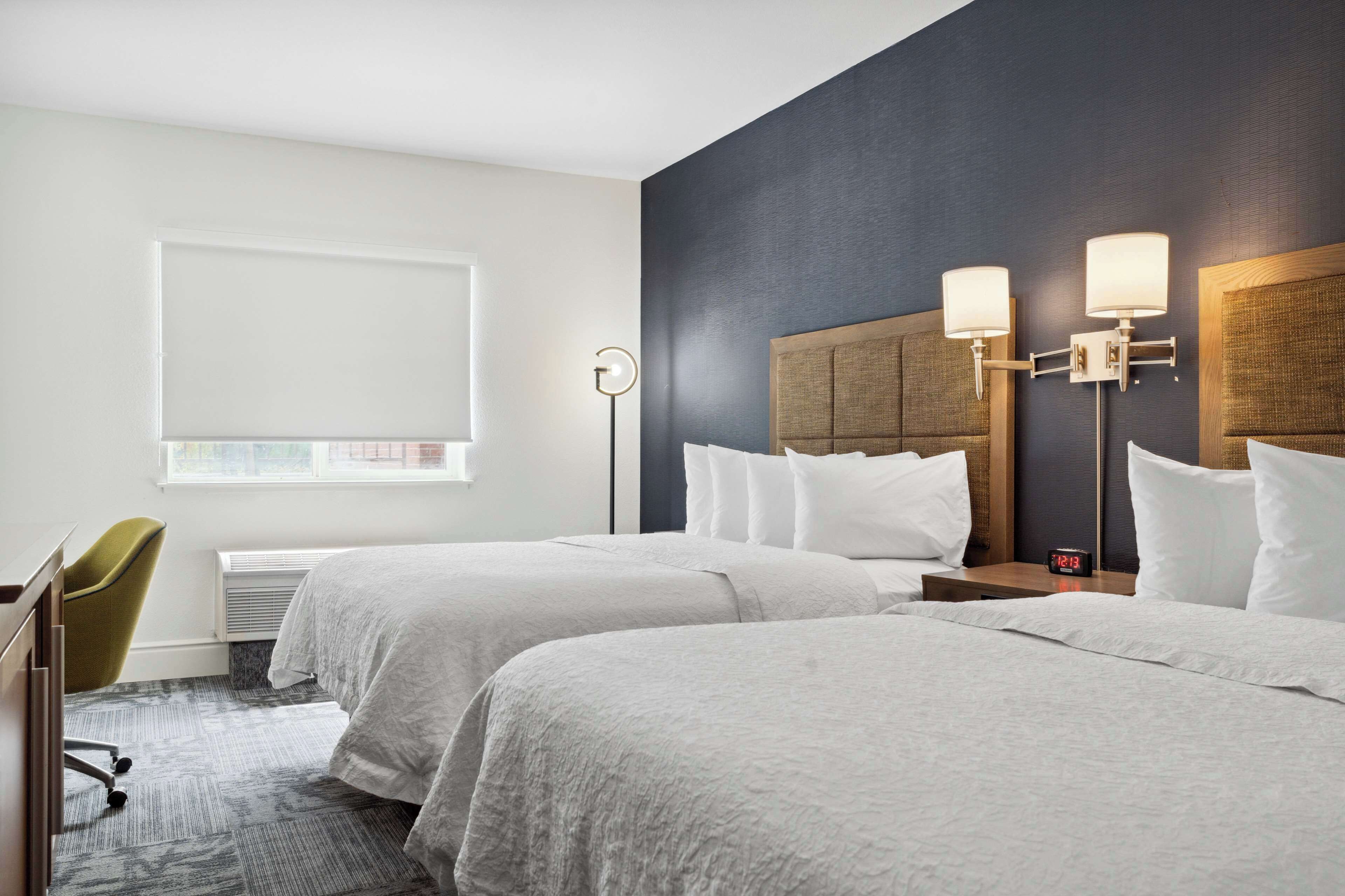 Habitación de hotel con dos camas, un escritorio, una silla, una ventana y una lámpara fijada a la pared.