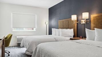 Habitación de hotel con dos camas, un escritorio, una silla, una ventana y una lámpara fijada a la pared.