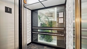An elevator interior with a glass door, a visible floor number '1', and a sign indicating the elevator direction. - Sonesta Essential Vacaville - Napa Valley (Vacaville)