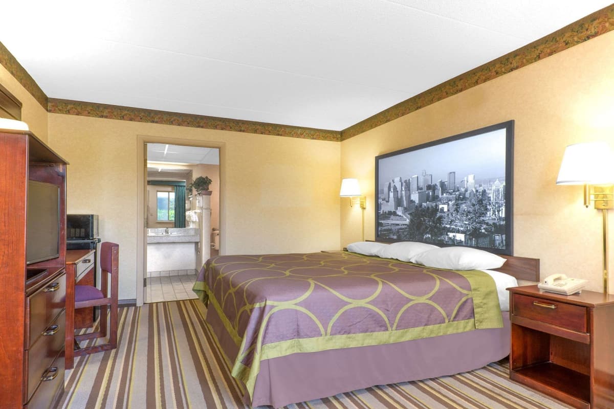 A hotel room with a bed, desk, chair, and a cityscape painting on the wall.