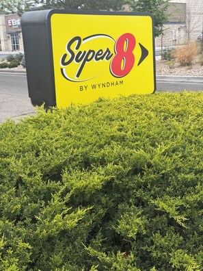 A sign for 'Super 8 by Wyndham' with a hedge in the foreground.