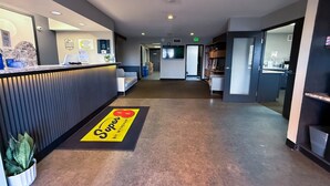 A hotel reception area with a reception desk, a waiting area with a sofa, a carpet with a logo, and a hallway leading to other rooms. - Super 8 by Wyndham Windsor (Windsor)