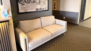 A reception area with a framed welcome sign, a sofa, a hand sanitizer dispenser, and a patterned carpet. - Super 8 by Wyndham Windsor (Windsor)