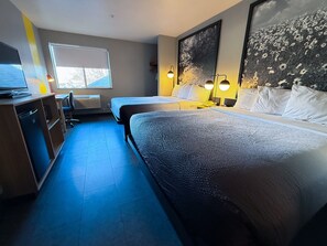 Habitación de hotel con dos camas, un escritorio, una silla, un televisor y un ventanal grande.
