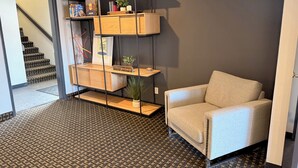 A hotel lobby with a staircase, a beige armchair, and a wooden shelving unit with various items. - Super 8 by Wyndham Windsor (Windsor)