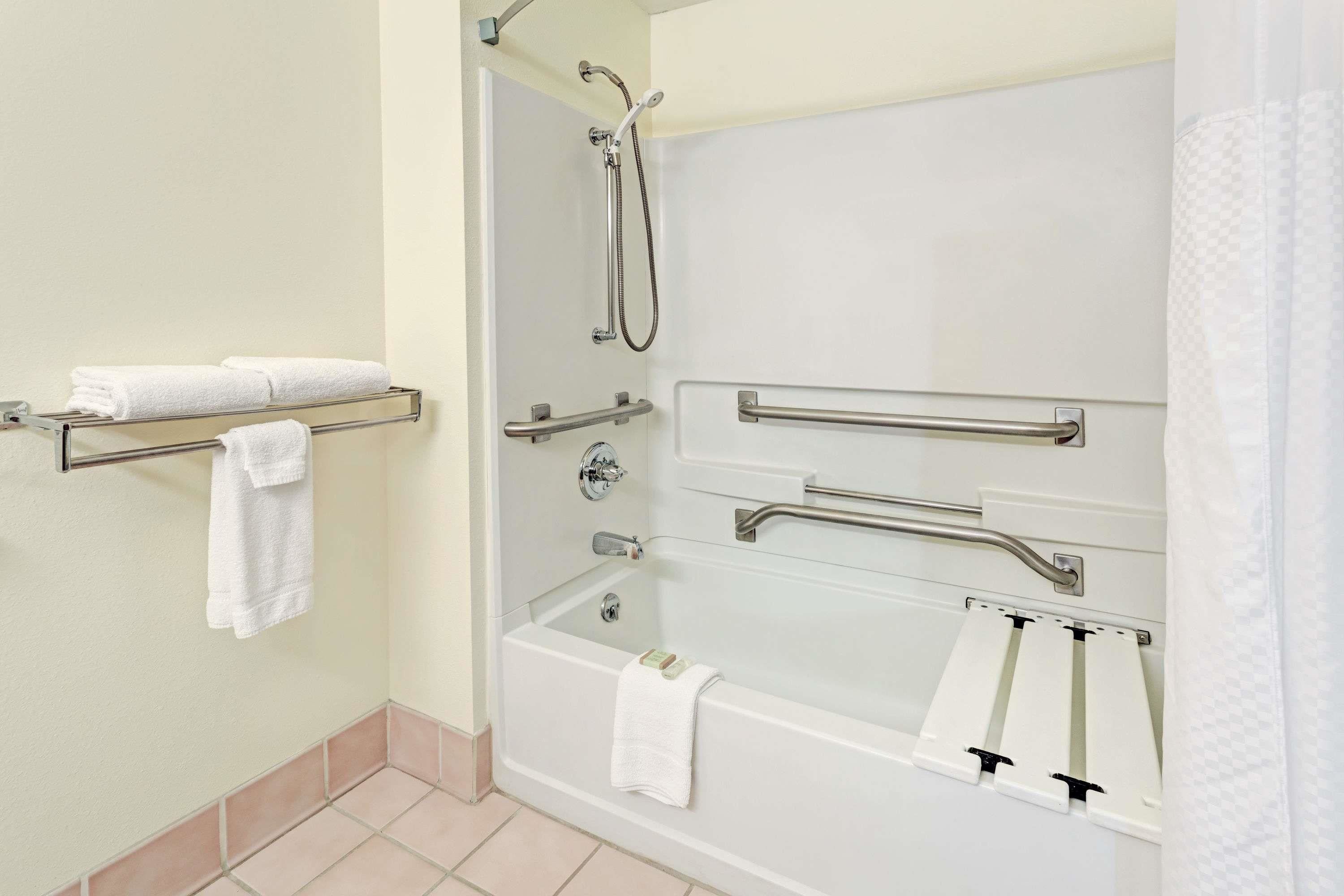 Un baño moderno con cabina de ducha, barras de apoyo y un perchero.