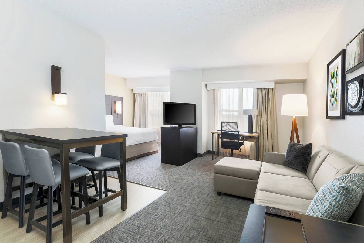 A hotel room with a dining area, a sofa, a TV, and a desk.