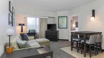 Una habitación de hotel moderna con un sofá, una mesa de comedor con sillas, un televisor sobre un mueble bajo y un mapa en la pared.