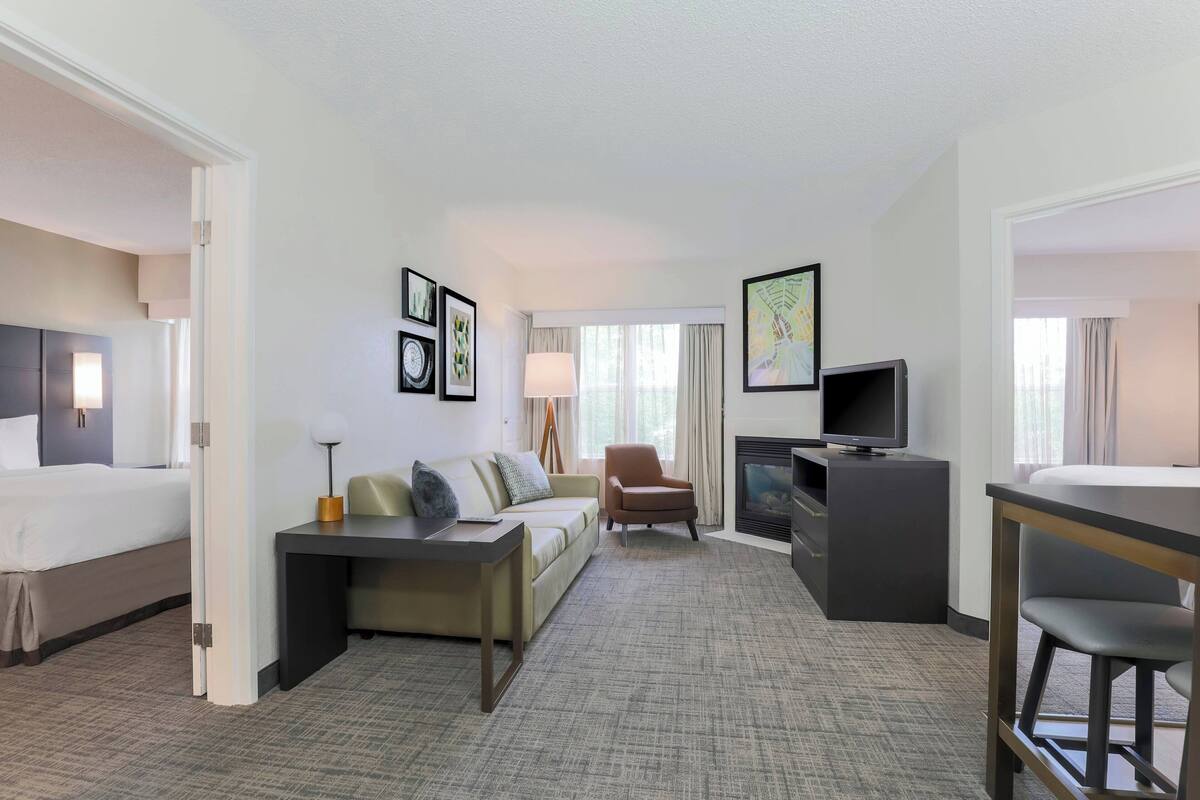 A hotel room with a bed, a sofa, a desk, a TV, and a fireplace.