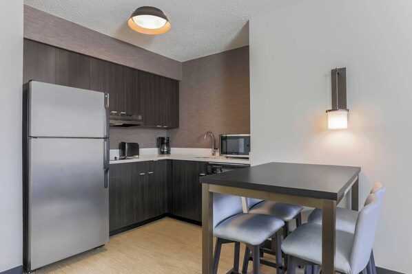 A modern kitchen with dark wood cabinets, a stainless steel refrigerator, a microwave, and a table with four chairs. - Residence Inn by Marriott Boulder Longmont (Longmont)