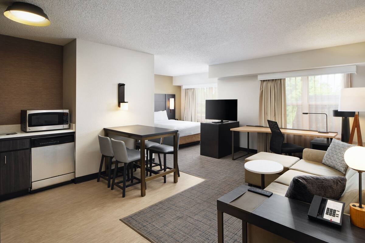 A hotel room with a kitchenette, a bed, a TV, a sofa, and a desk.