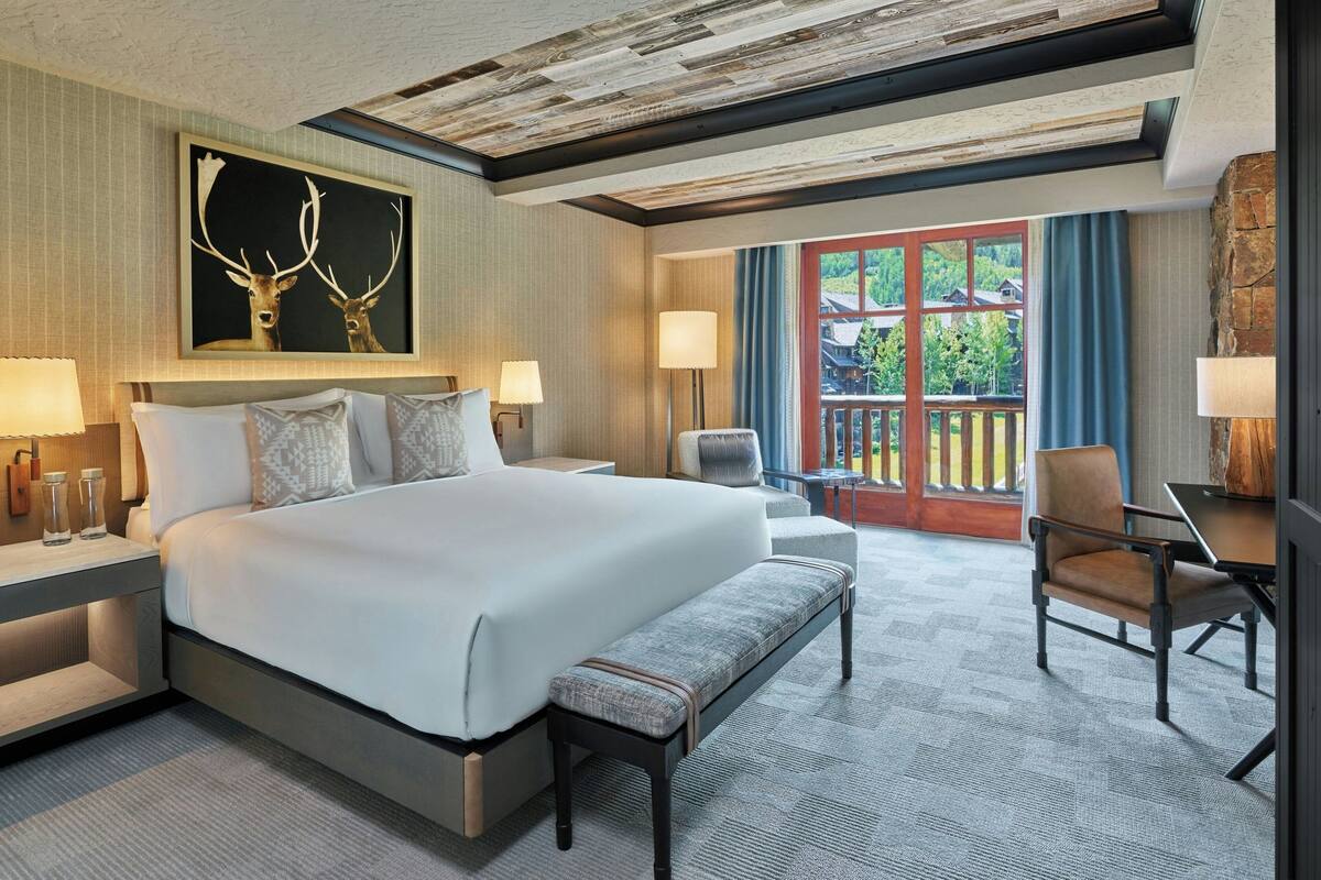 Ein geräumiges Hotelzimmer mit einem großen Bett, einer Sitzbank, einem Schreibtisch und Blick ins Freie.