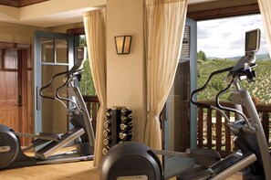 An indoor exercise area with stationary bikes and a treadmill, a wooden door, and a view of greenery through a window.