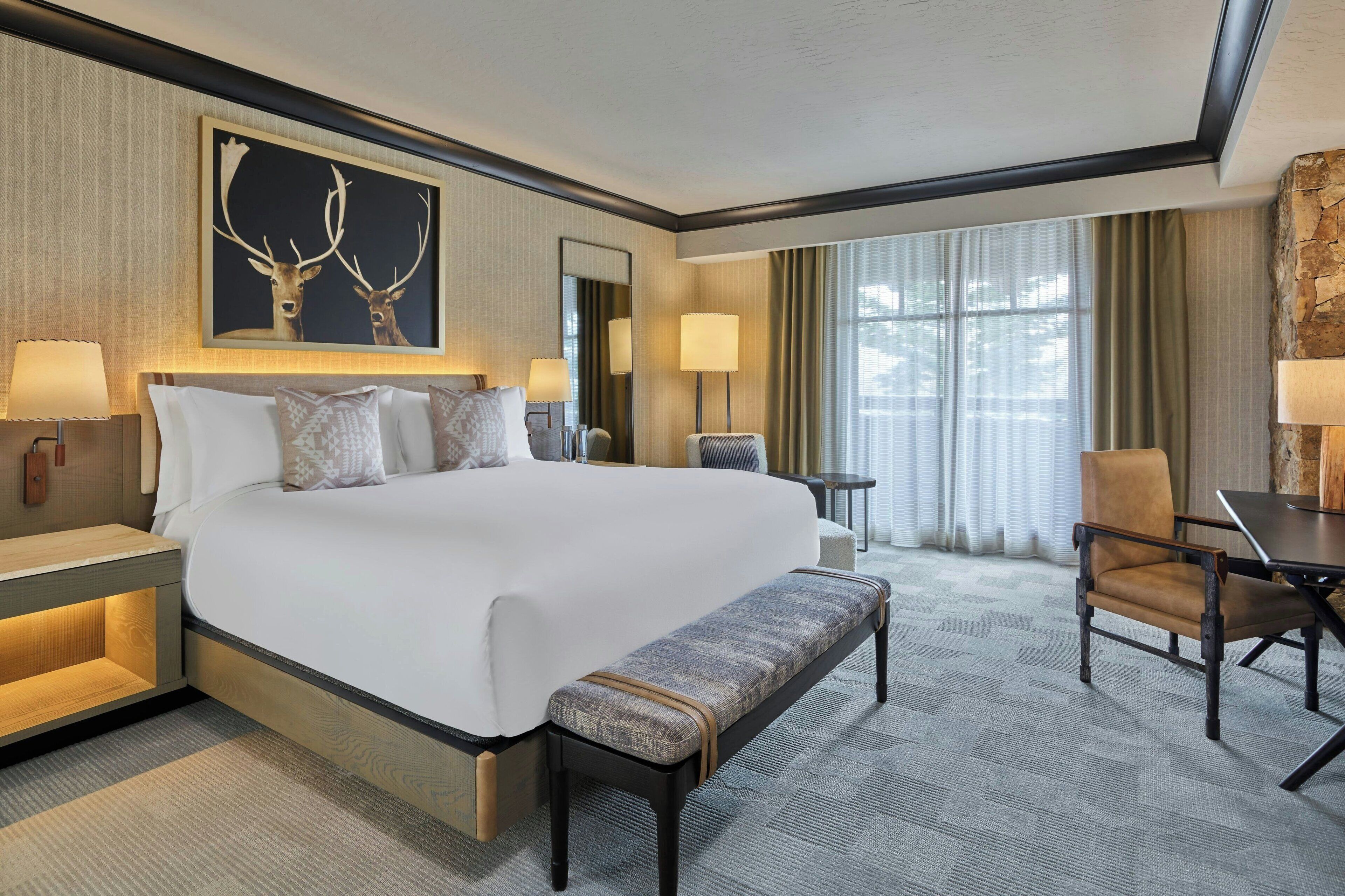 A hotel room with a large bed, a bench, a desk, and a chair.