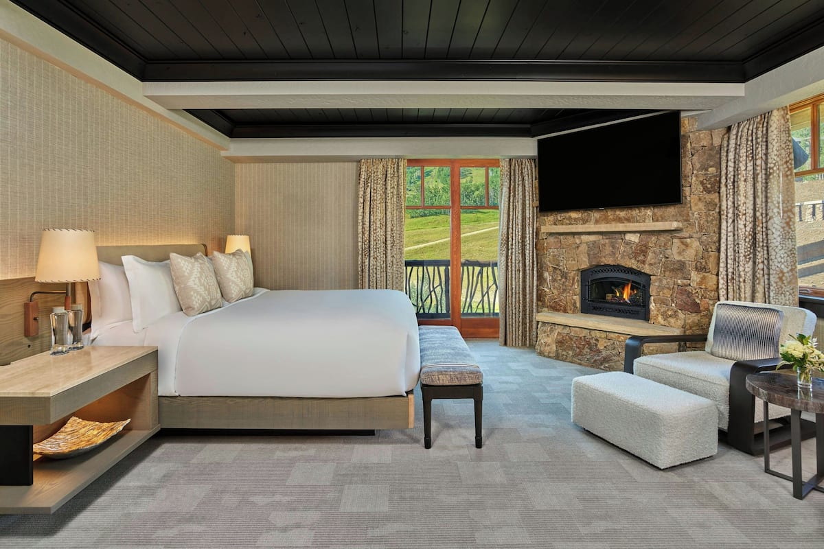 Ein geräumiges Schlafzimmer mit einem großen Bett, einem Kamin aus Stein, einem Flachbildfernseher und einem Balkon mit Blick ins Freie.