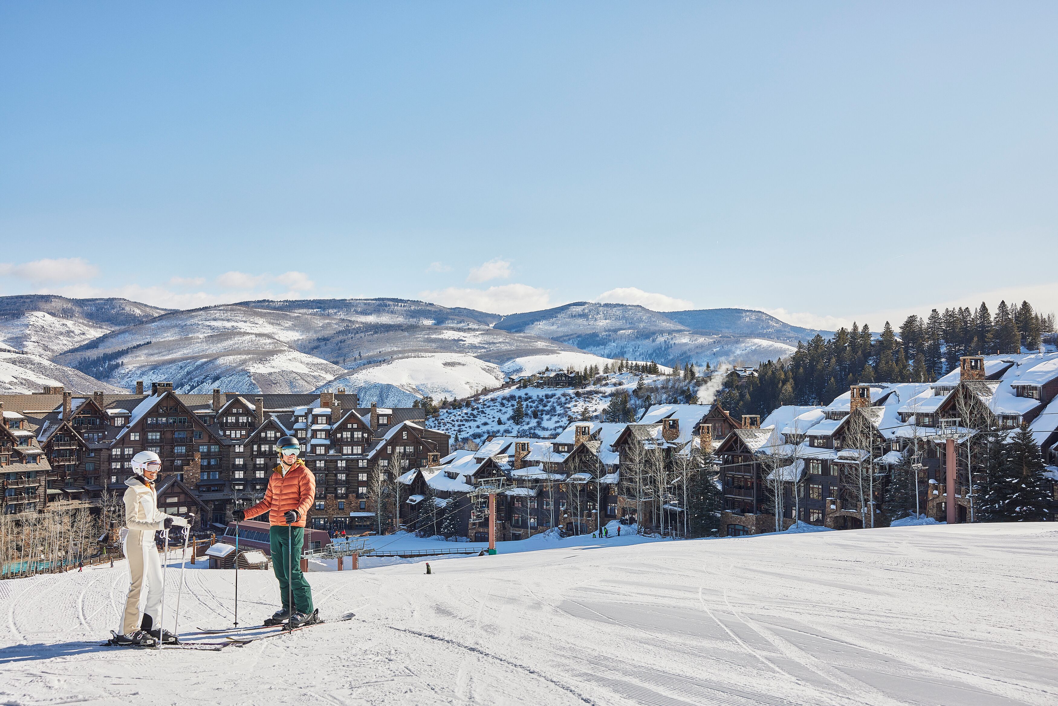A ski resort with traditional wooden buildings, a clear sky, and snow-covered terrain.