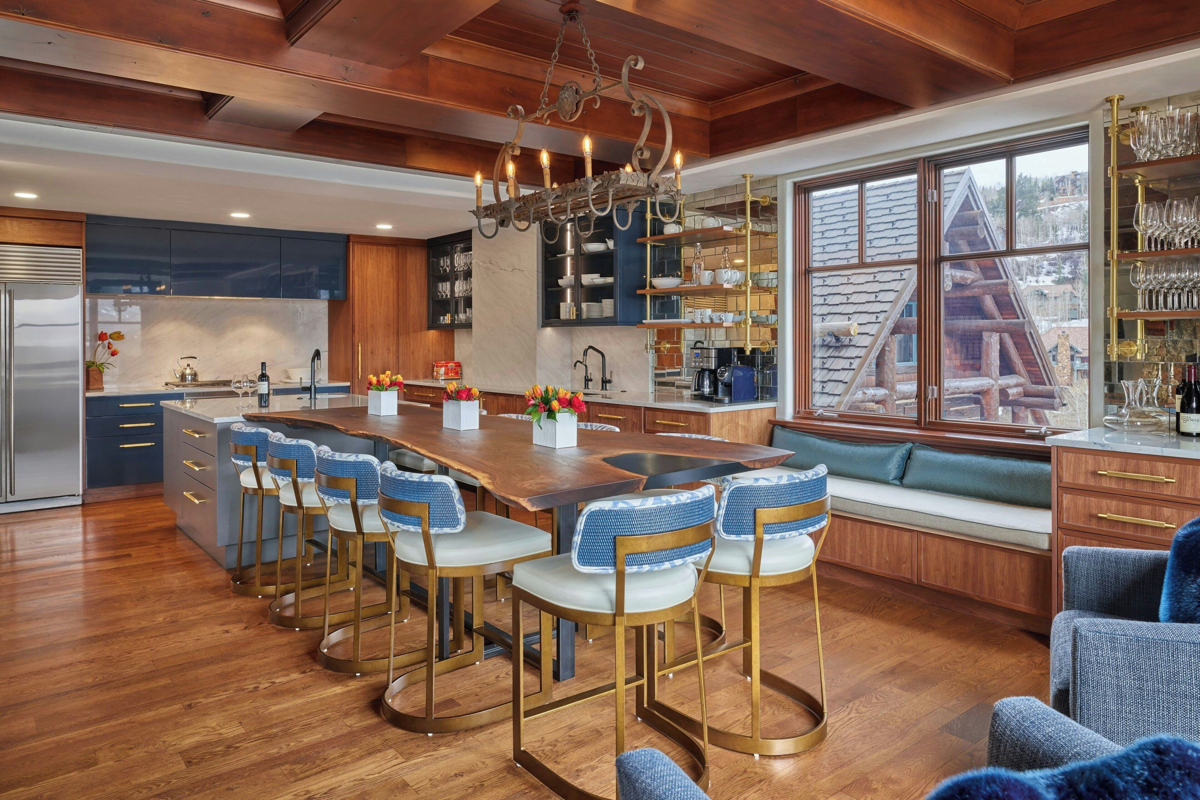A modern kitchen with a central island, bar stools, and a view of a cabin through large windows.