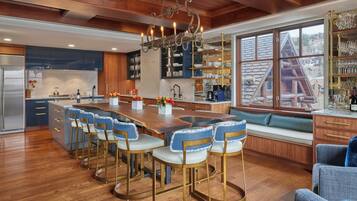 A modern kitchen with a central island, bar stools, and a view of a cabin through large windows.